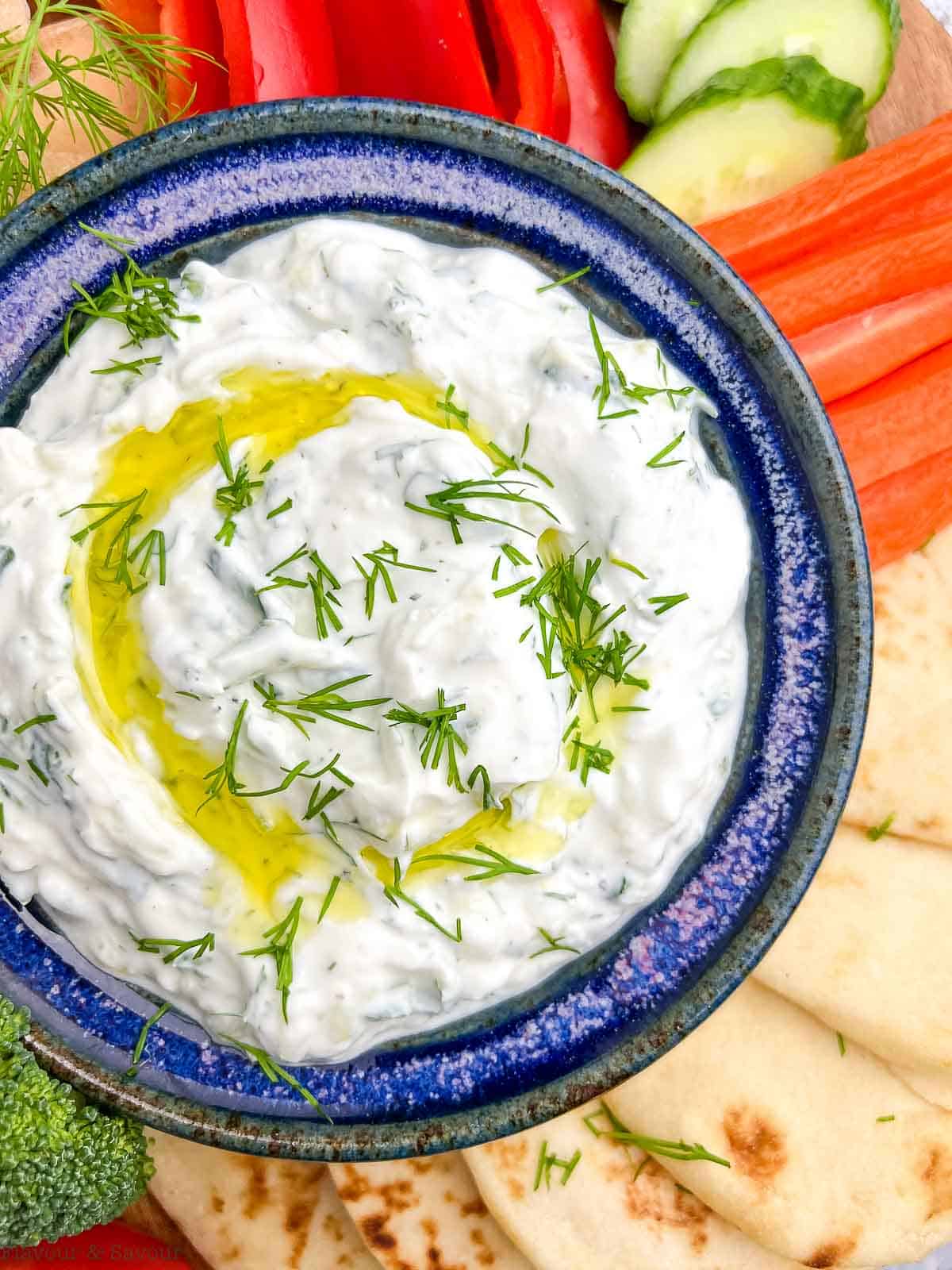 Close up view of a bowl of tzatziki sauce drizzled with olive oil and sprinkled with fresh dill.