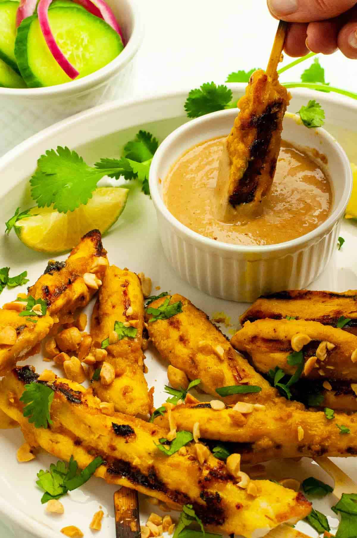 Skewers of chicken satay topped with chopped peanuts and cilantro leaves.