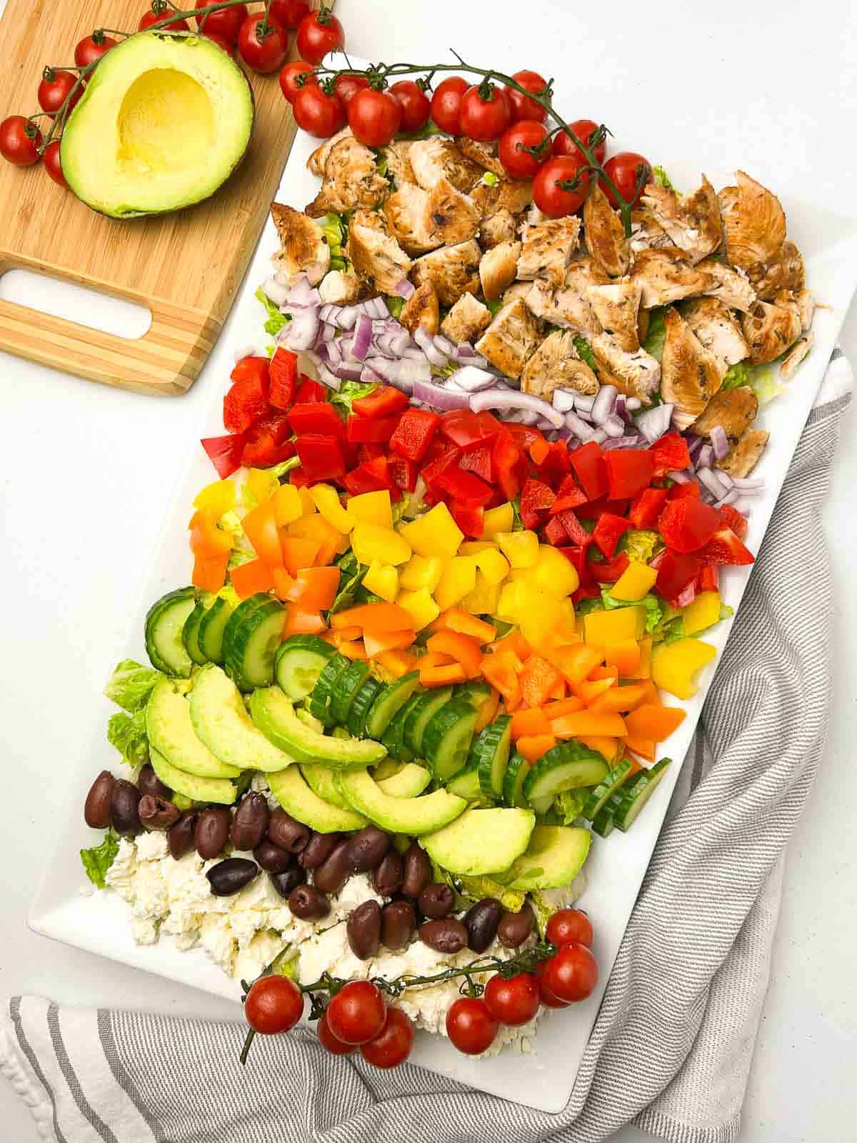 Greek Chicken Cobb Salad with rows of chicken, vegetables, olives and feta cheese on top of a bed or romaine.