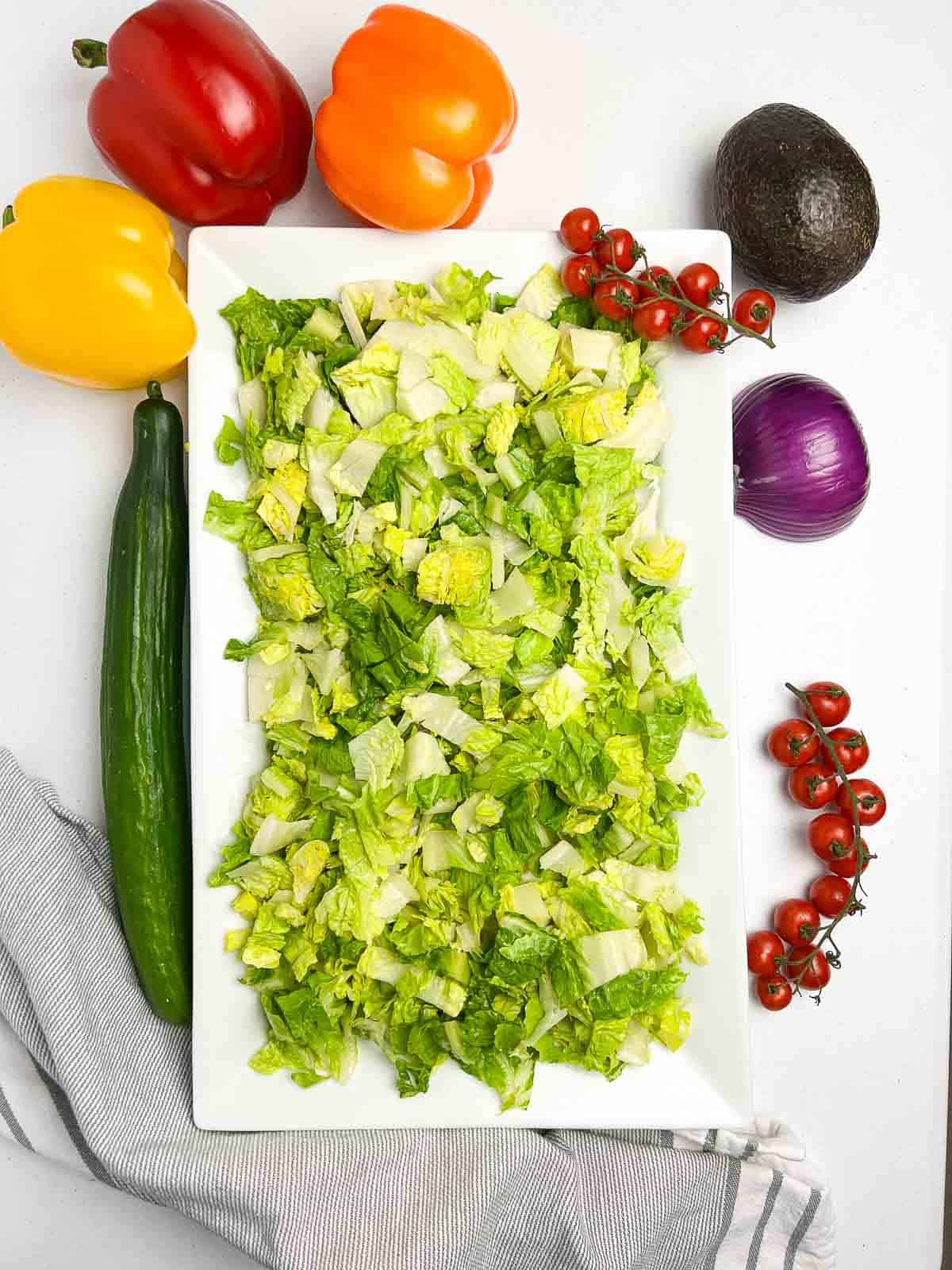 Preparing Greek Chicken Cobb Salad by starting with a bed of romaine lettuce.