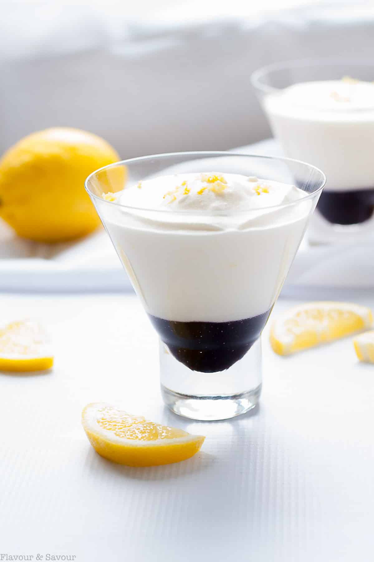 Light lemon mousse with blueberry sauce in a dessert glass garnished with lemon zest.