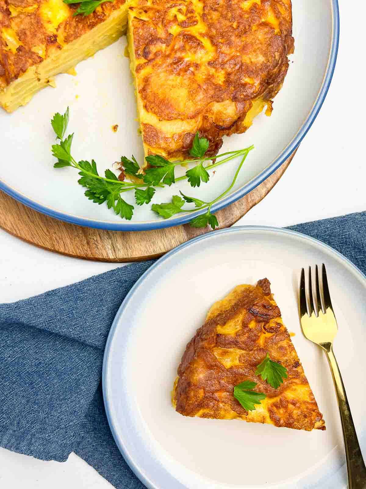 A wedge of Spanish tortilla on a plate with a fork with the remainder of the tortilla beside it.