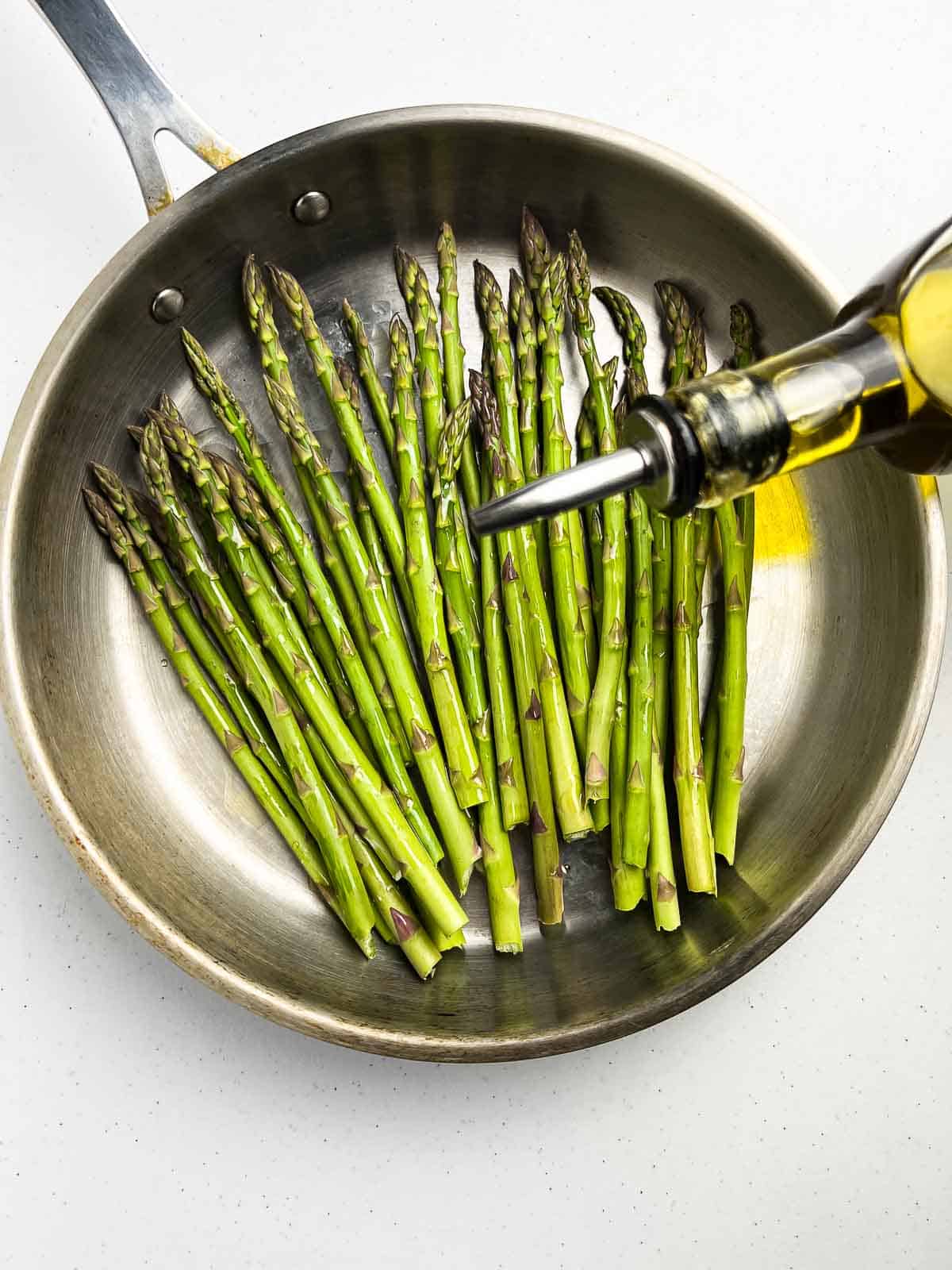 Asparagus spears in a skillet with olive ol.
