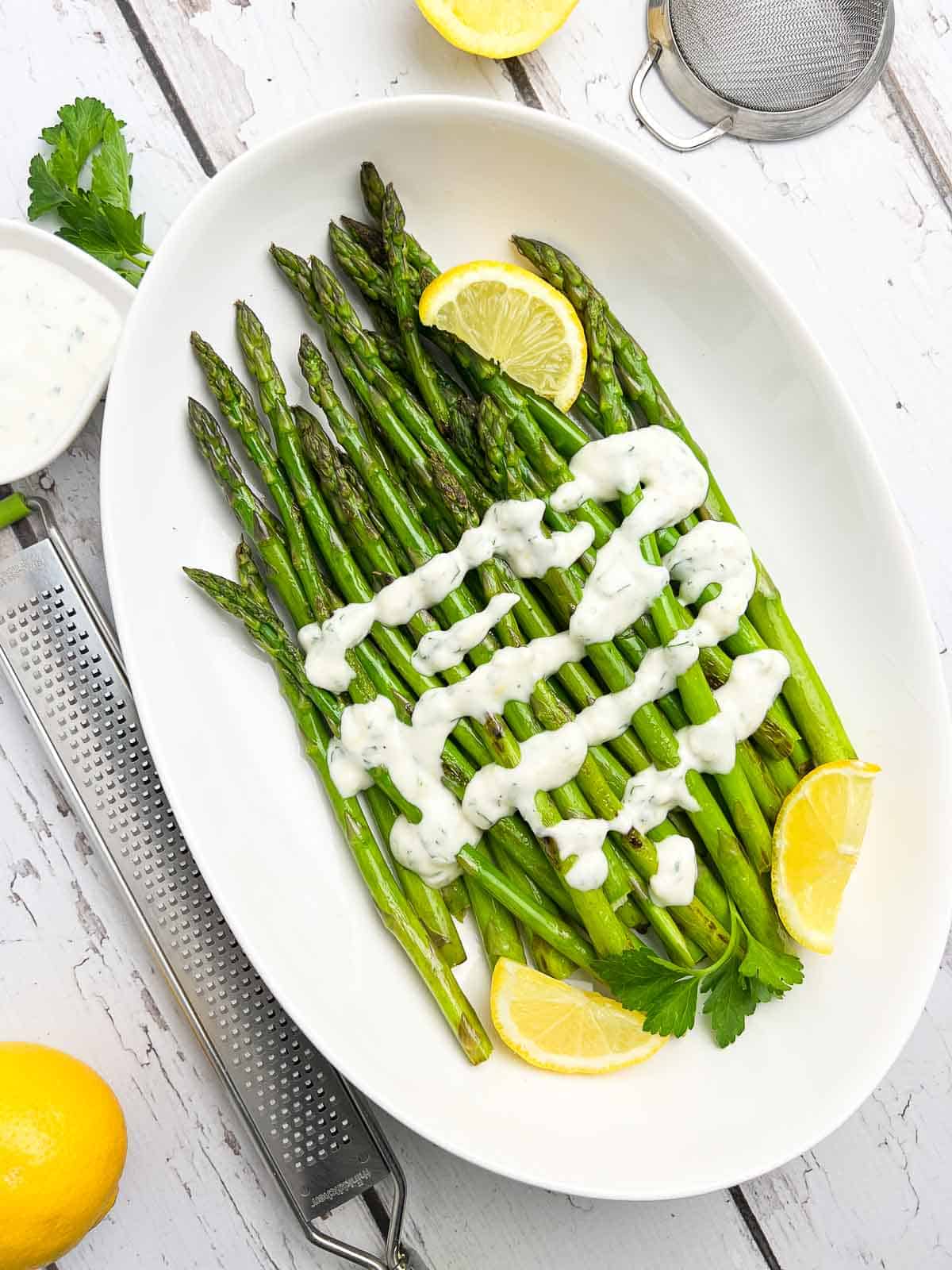 A bowl of asparagus topped with lemon aioli with a microplane nearby.