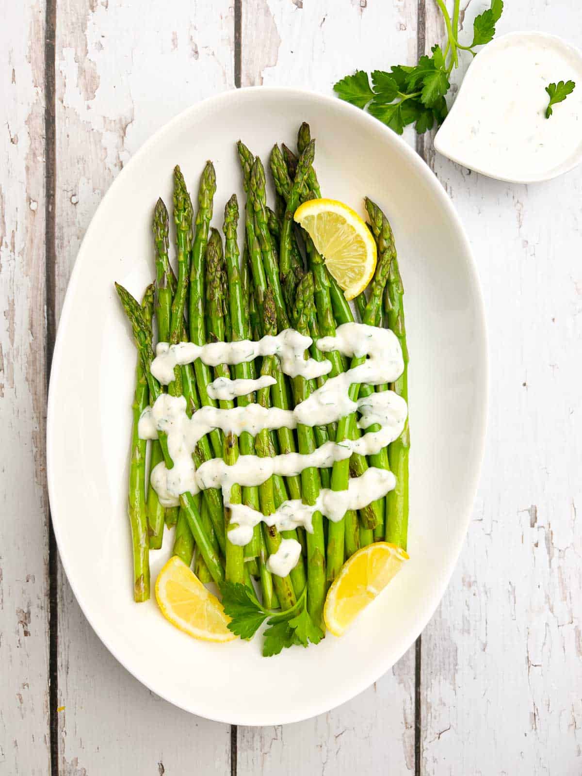 Overhead view of a white serving bowl with asparagus spears drizzled with lemon aioli.