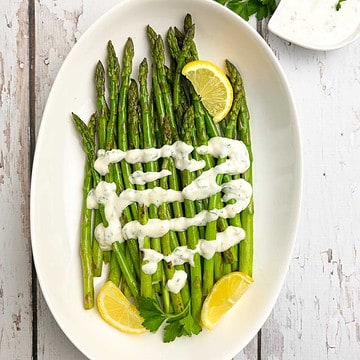 A bowl of asparagus topped with lemon aioli and lemon wedges.