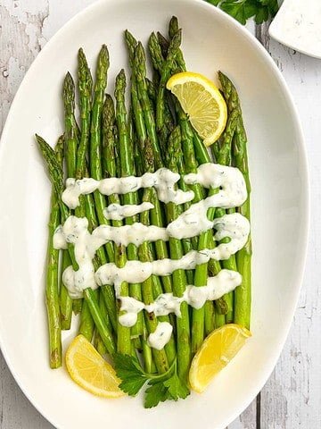 A bowl of asparagus topped with lemon aioli and lemon wedges.