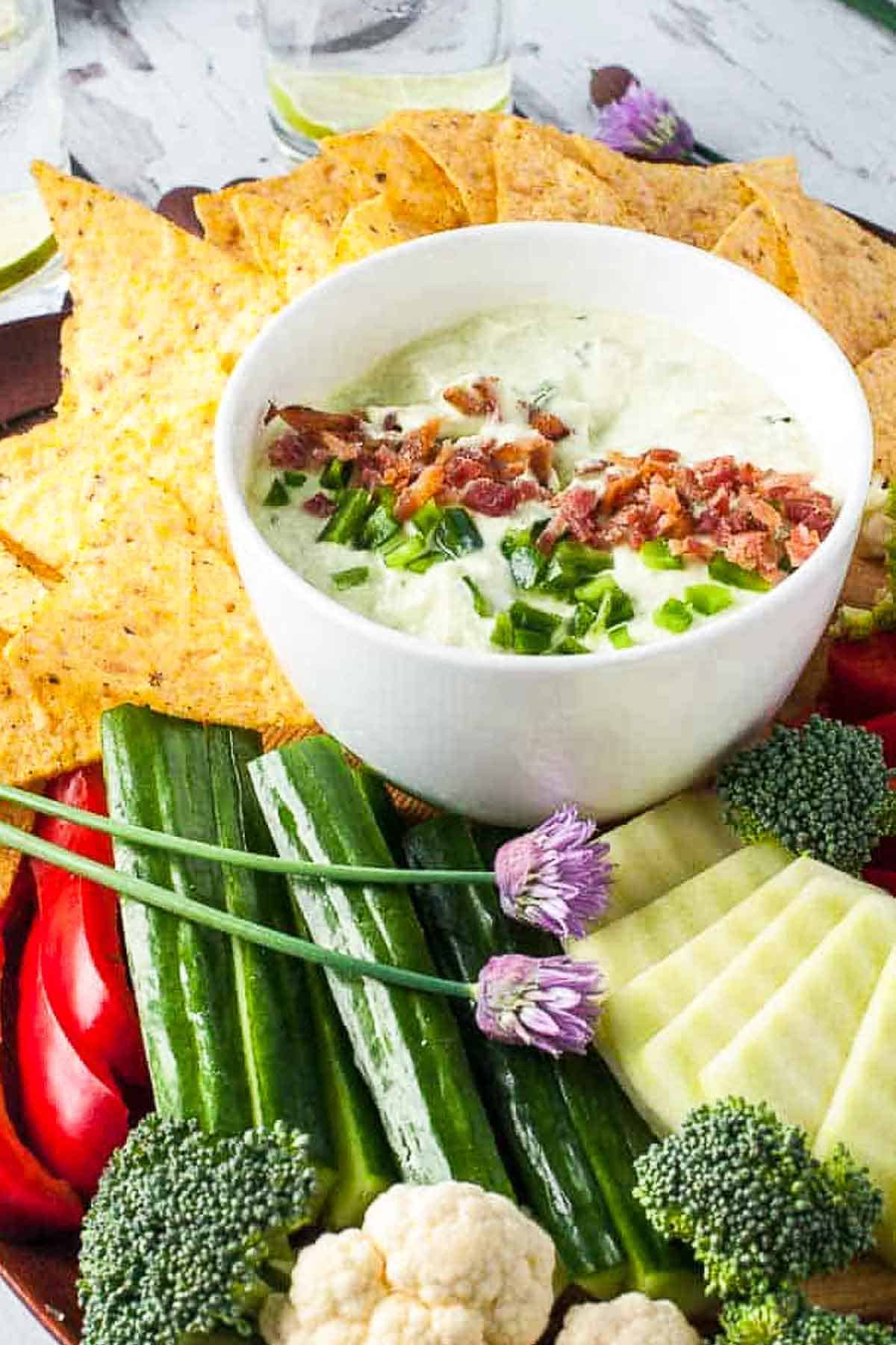 A bowl of bacon and chive dip with jalapeños surrounded by fresh veggies for dipping.