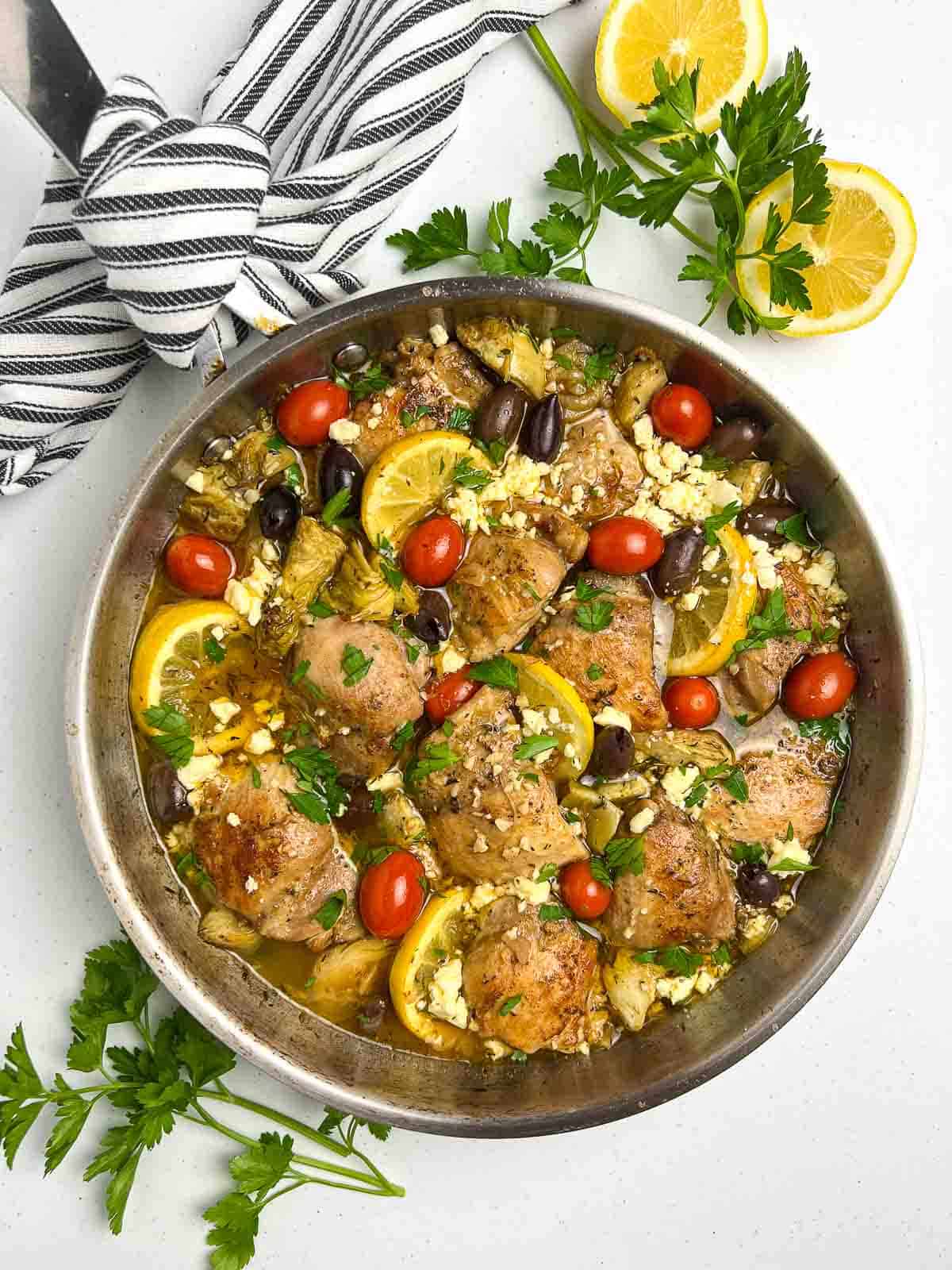 Baked Lemon Artichoke Chicken with olives and tomatoes in a skillet.
