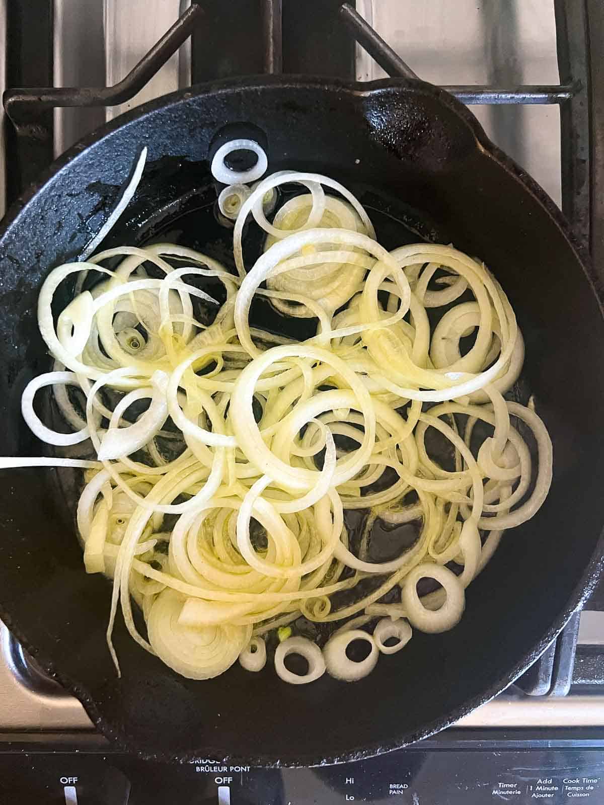 Onions sautéing in a cast iron skillet for Spanish tortilla.