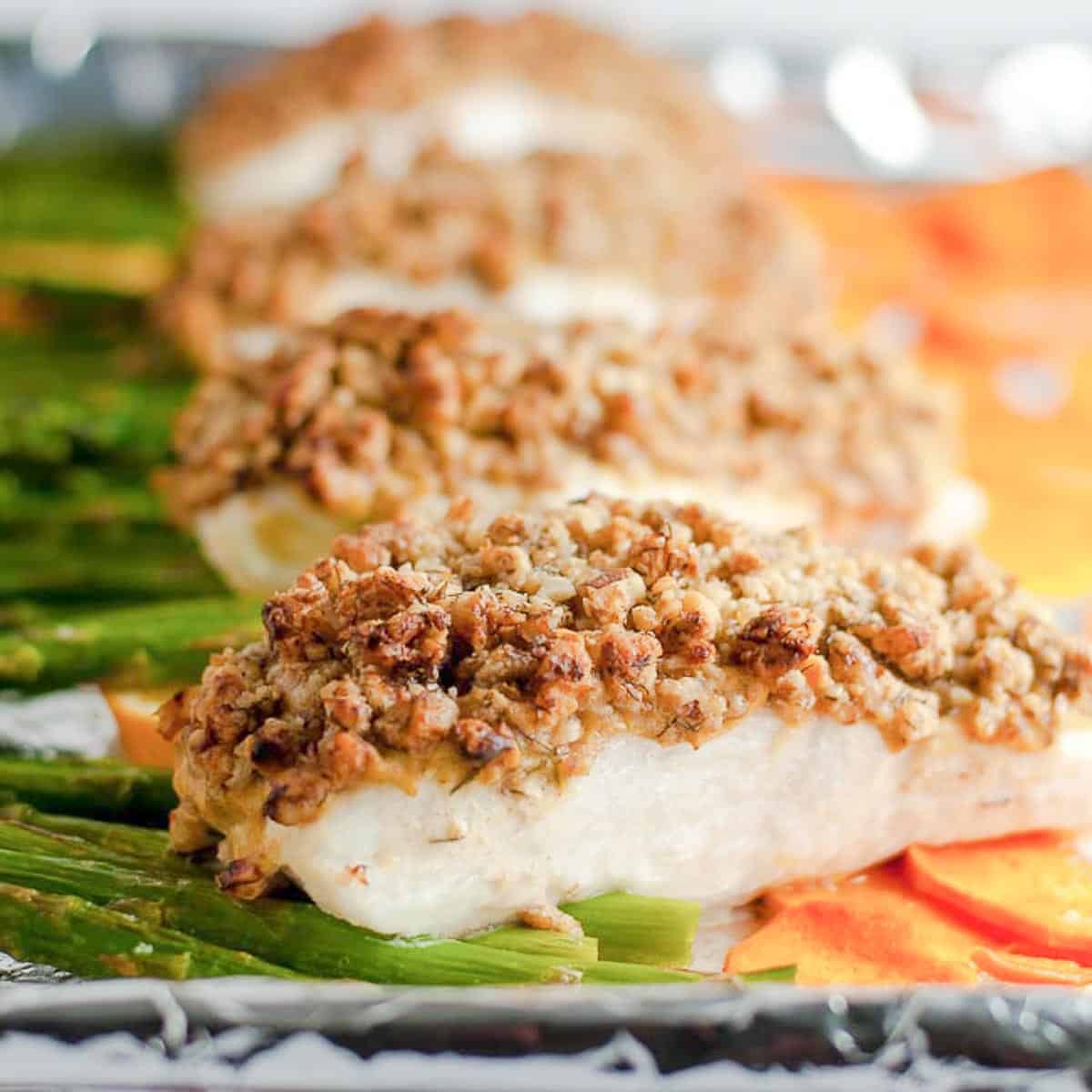 Halibut fillets on a sheet pan with asparagus spears and thin sweet potato slices.