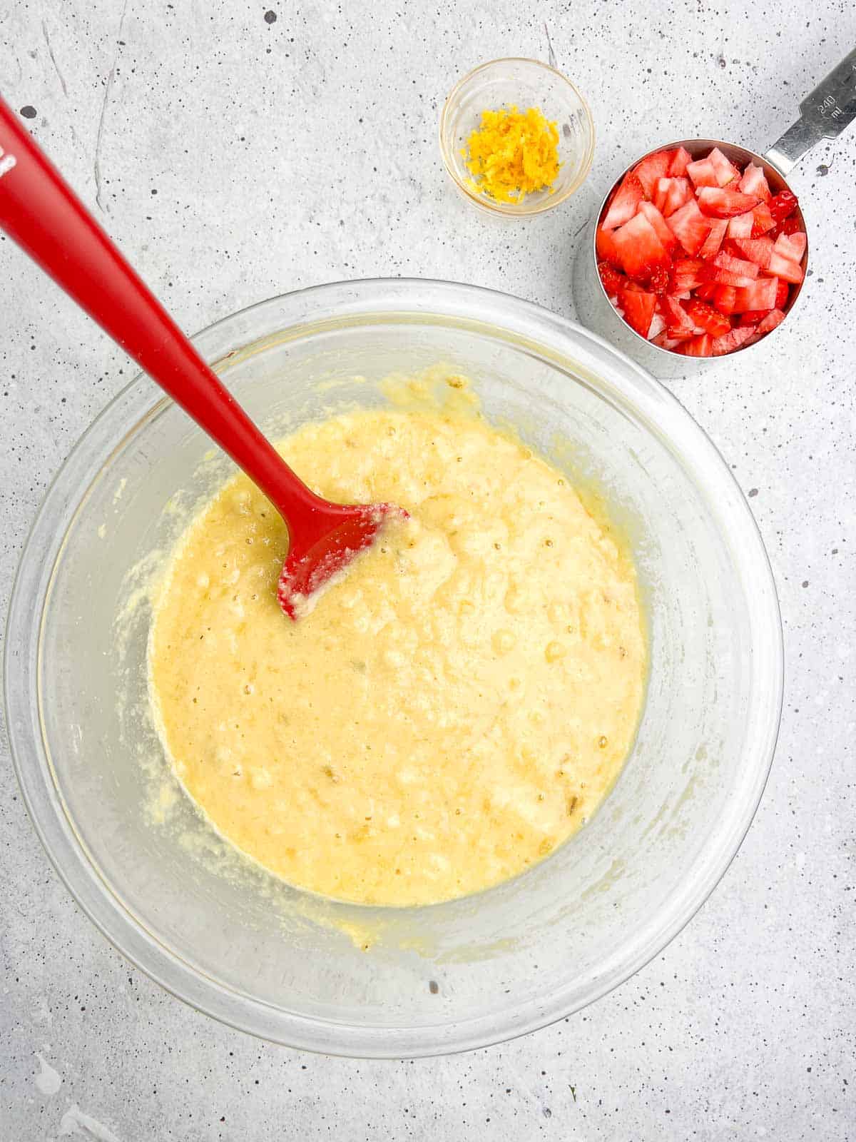 Combined dry and wet ingredients for banana bread with strawberries in a glass bowl.