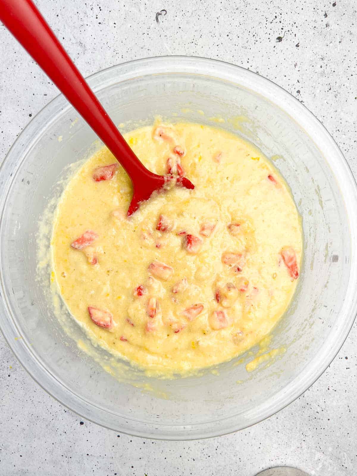 Preparing strawberry banana bread by gently folding in diced strawberries and lemon zest.