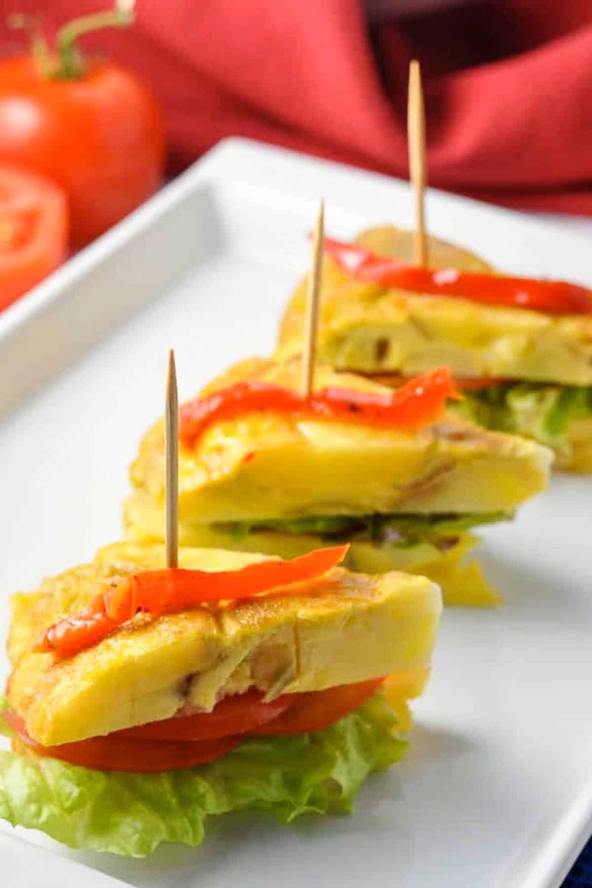 Tortilla Española sliced horizontally and filled with lettuce, tomato and aioli.
