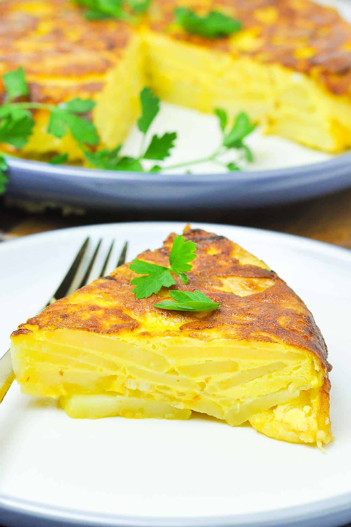 A slice of traditional Spanish tortilla or Tortilla Española on a plate with a fork.