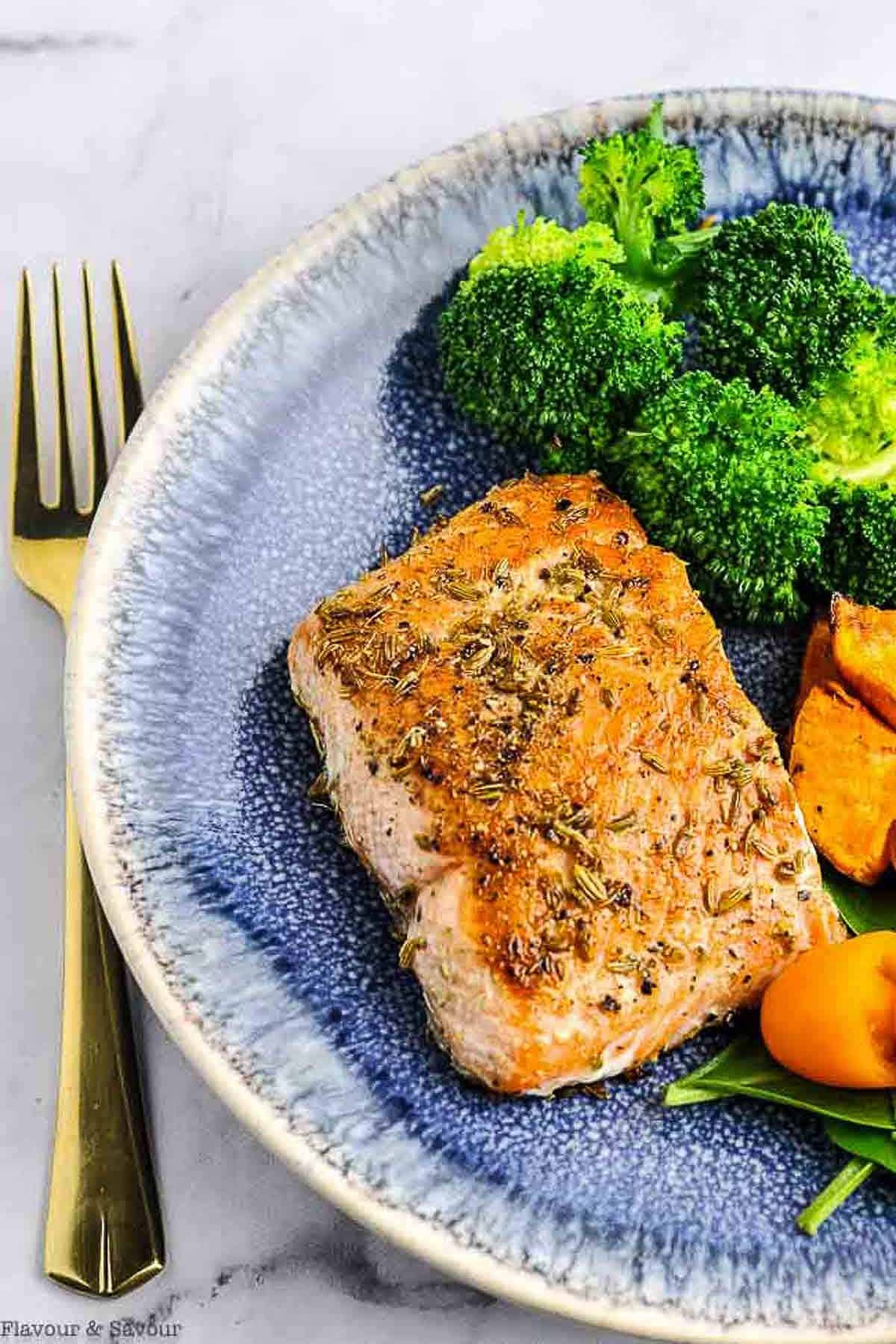 Fennel crusted salmon fillet on a blue plate with broccoli and roasted sweet potato cubes.