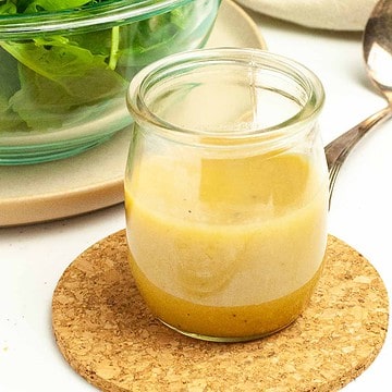A small jar of Honey-Dijon Vinaigrette Dressing with a salad in the background.