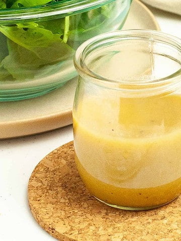 A small jar of Honey-Dijon Vinaigrette Dressing with a salad in the background.