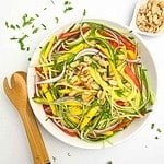 A bowl of Thai mango salad with a pair of bamboo tongs beside it.