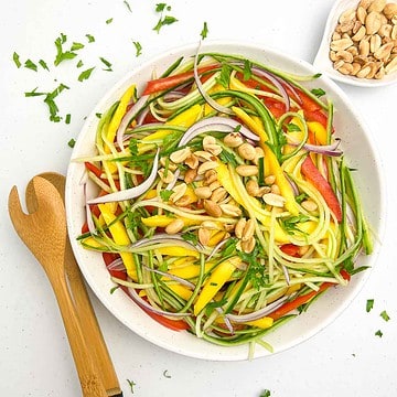 A bowl of Thai mango salad with a pair of bamboo tongs beside it.