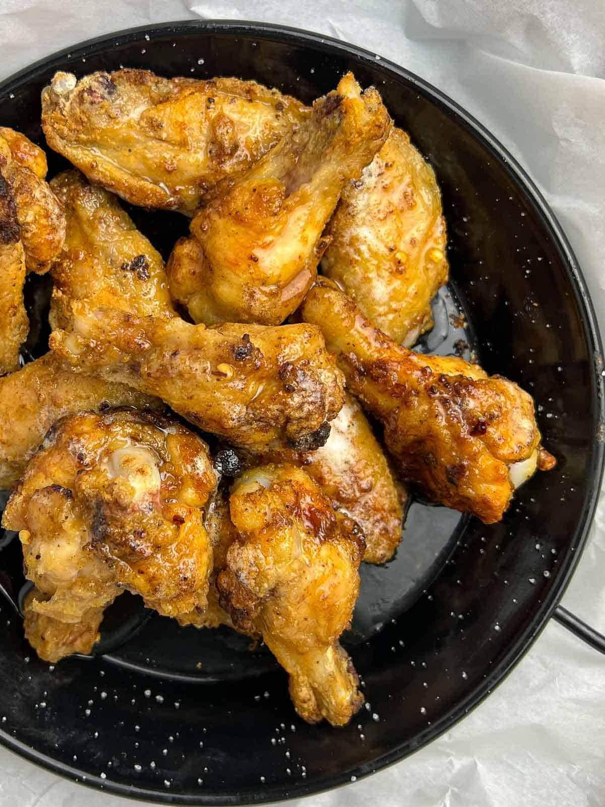 Close up view of hot honey chicken wings in a black serving dish.