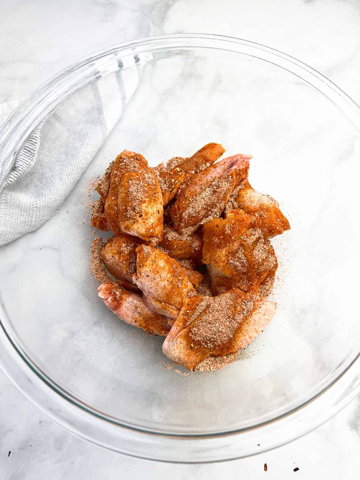 Chicken wings in a glass bowls tossed with poultry seasoning.