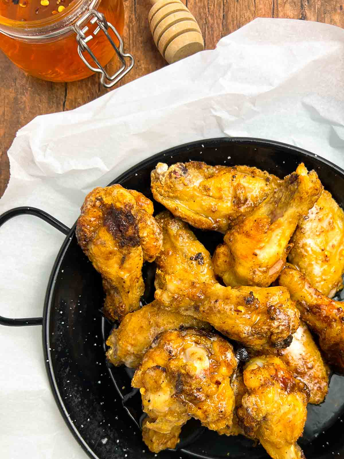 A plate of air fryer hot honey wings with a small jar of hot honey beside.
