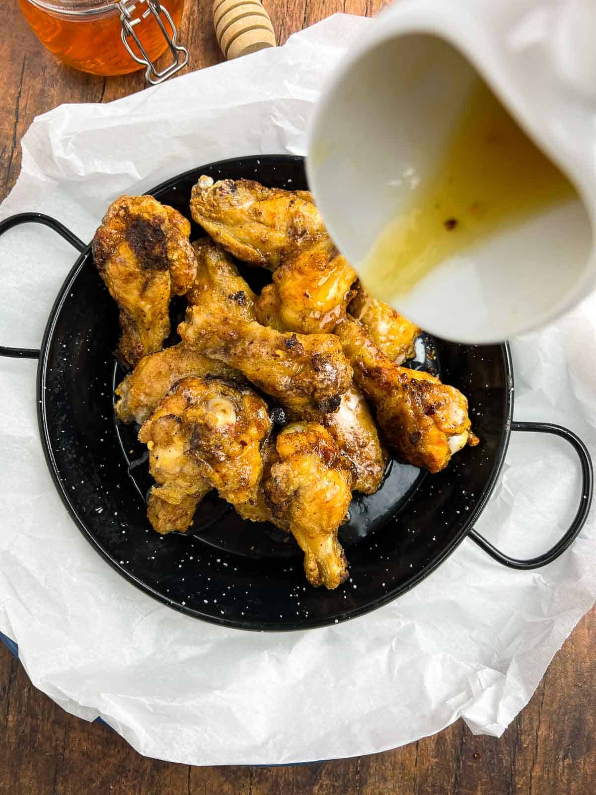 Pouring hot honey on cooked chicken wings.