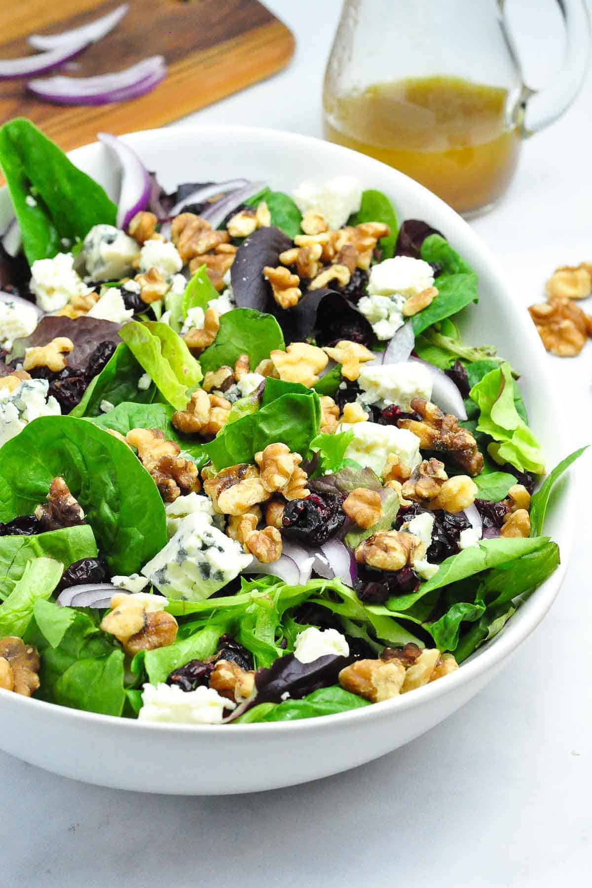 Side view of blue cheese walnut salad in an oval bowl with a small jar of maple balsamic dressing.