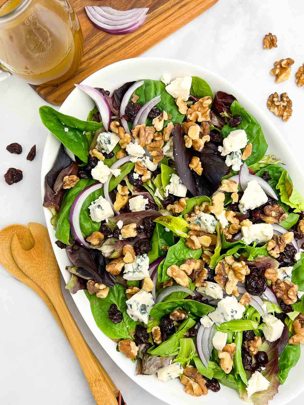 Overhead view of a white bowl filled with a green salad with blue cheese, walnuts and cranberries.