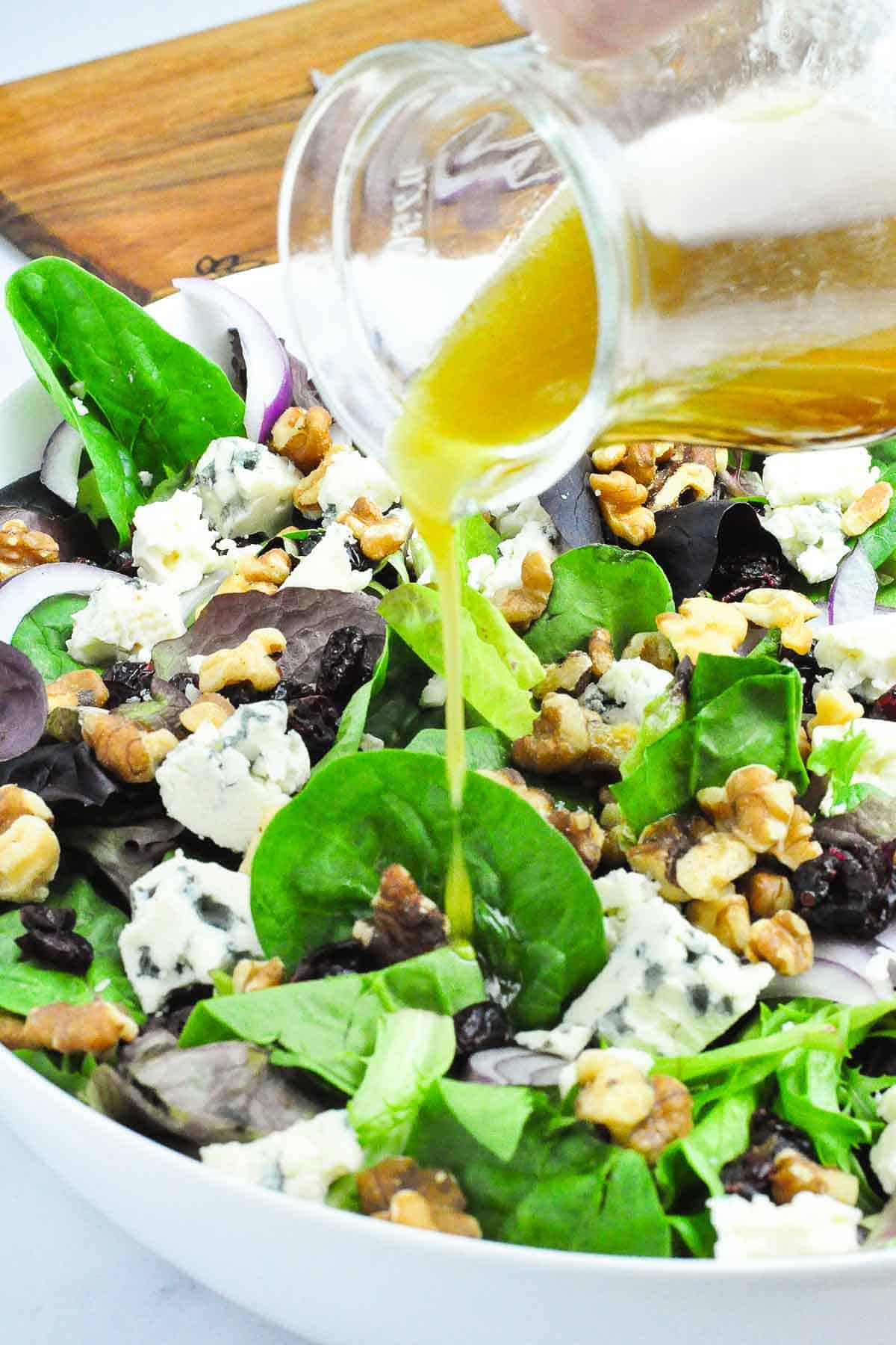 Drizzling maple balsamic dressing on to a salad made with blue cheese and walnuts.