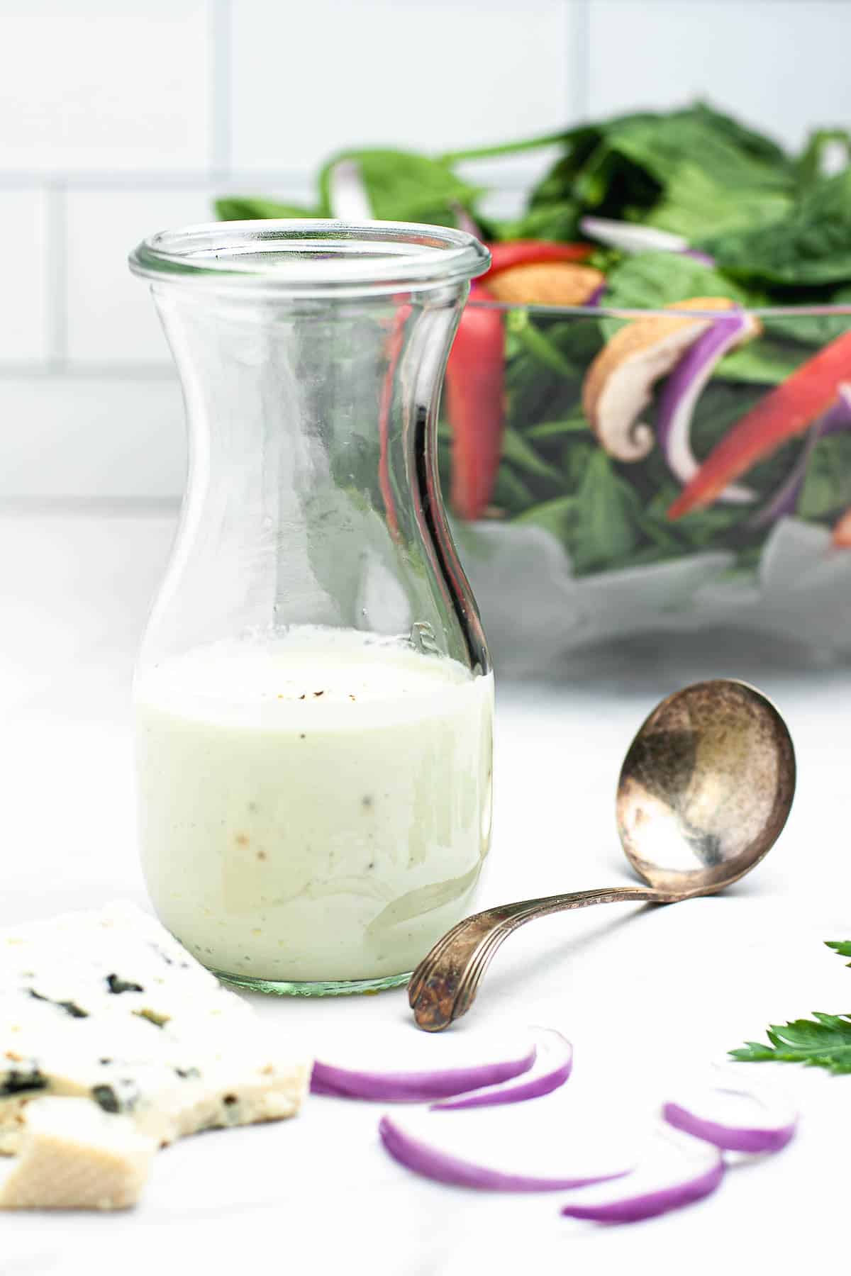 A Weck jar with Greek yogurt Gorgonzola dressing and a salad in the background.