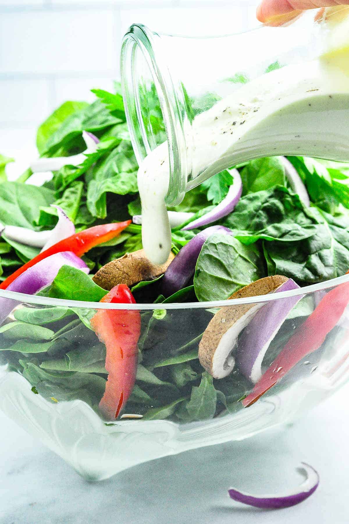 Pouring Gorgonzola dressing on a green salad in a glass bowl.