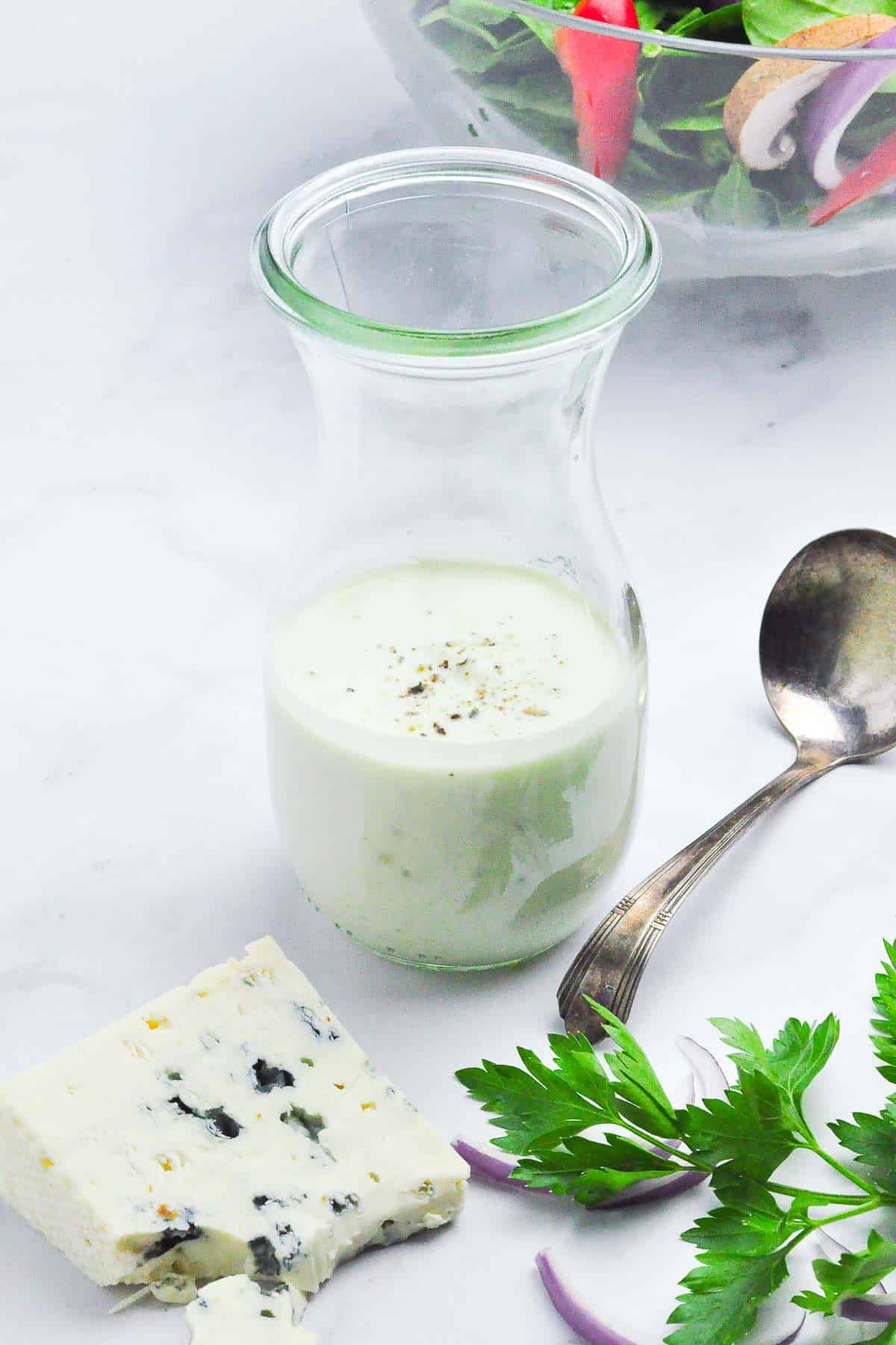 Close up view of a jar of Gorgonzola dressing with a block of blue cheese in the foreground.