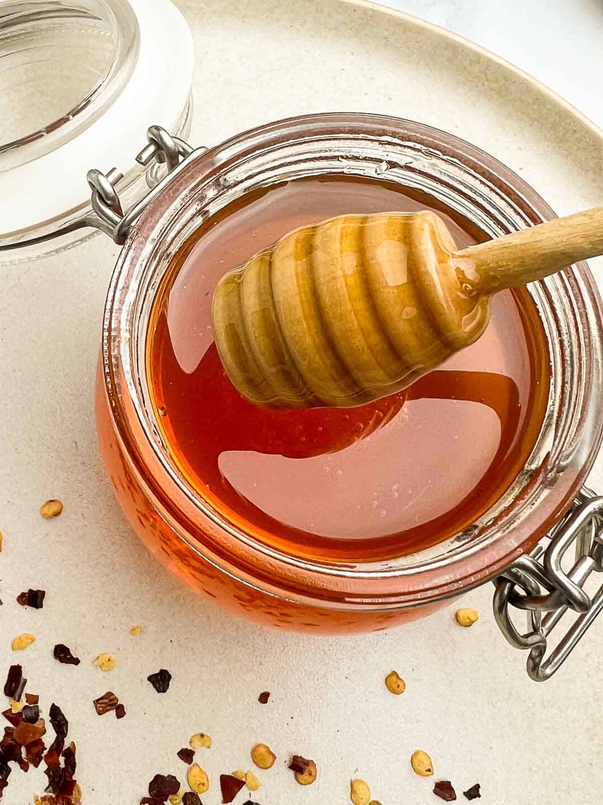 A jar of honey infused with dried red pepper flakes with a honey dipper.