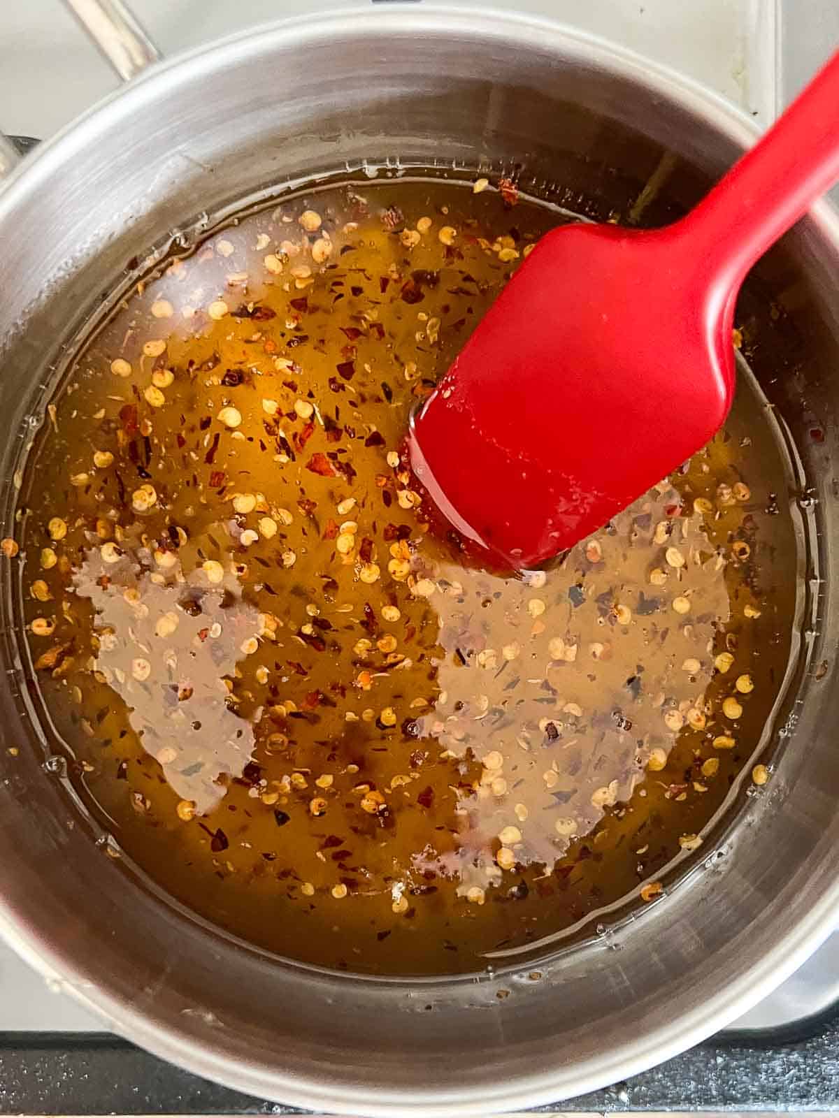 Hot honey simmering in a saucepan with crushed red pepper flakes.
