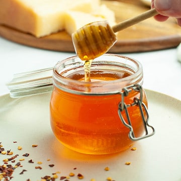 A small Weck jar with hot honey drizzling from a honey dipper.