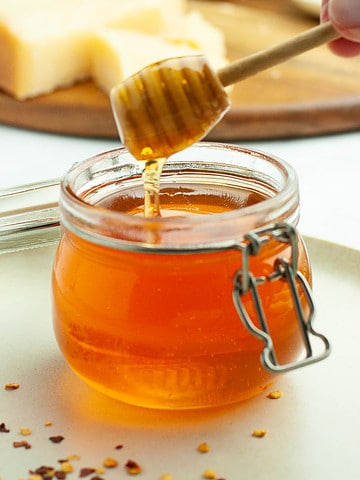 A small Weck jar with hot honey drizzling from a honey dipper.