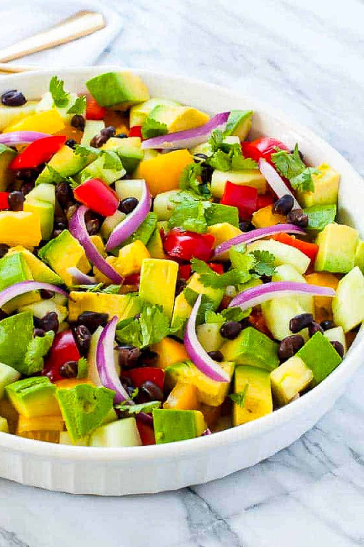 A bowl of black bean salad with tomatoes, avocados and red onions with cilantro lime dressing.