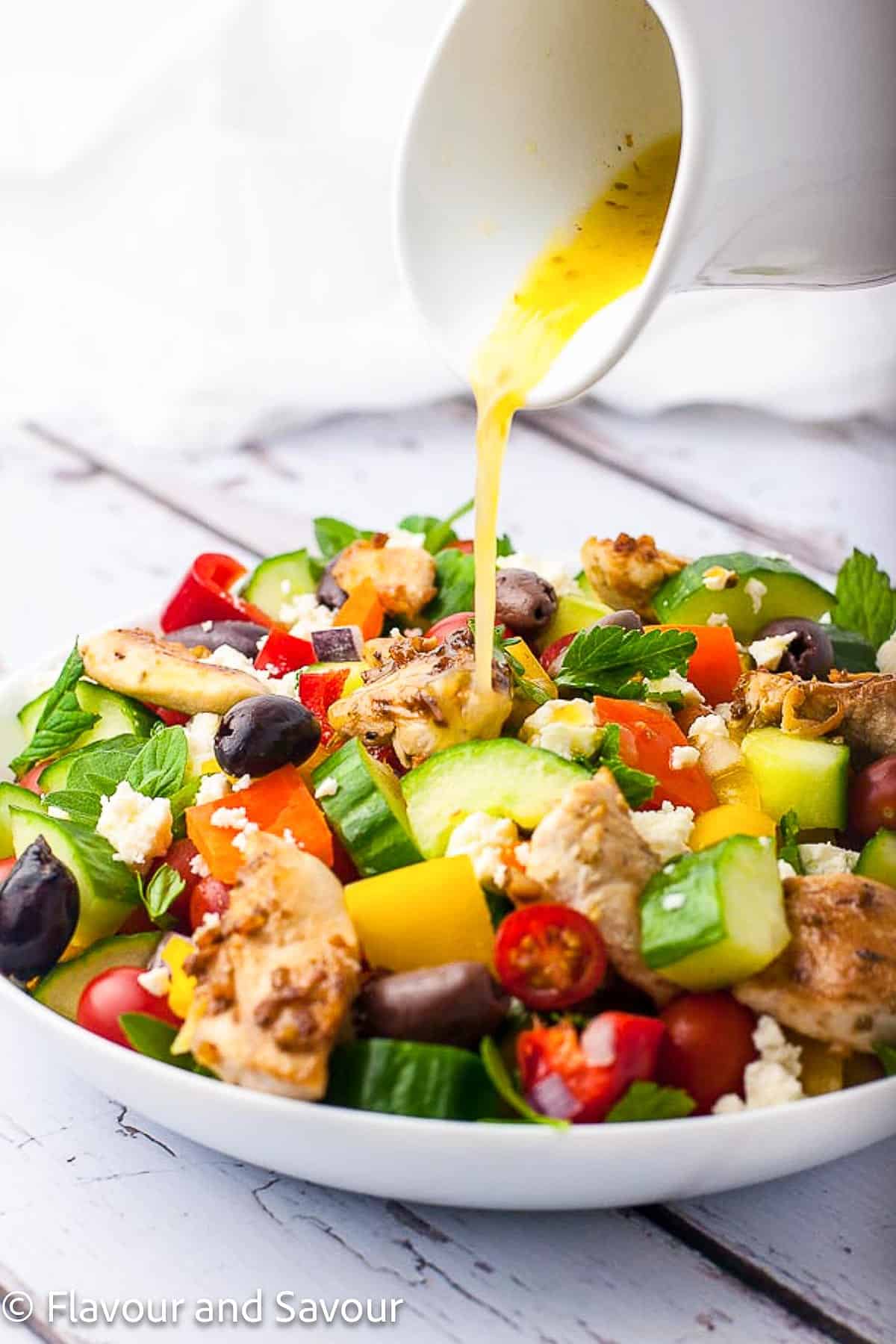 Adding dressing to Greek salad with grilled chicken.