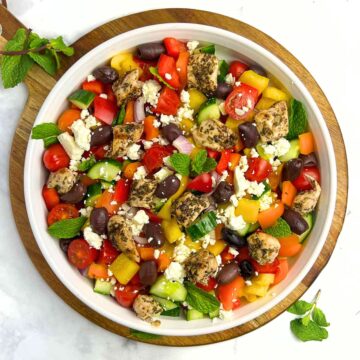 Overhead view of a round shallow bowl with Greek Chicken Salad with Mint leaves.