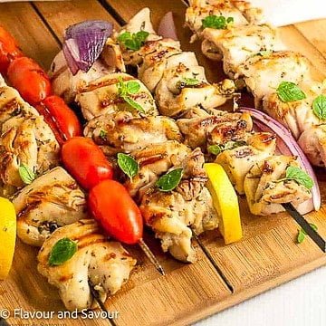 Greek lemon chicken kabobs on skewers on a board.