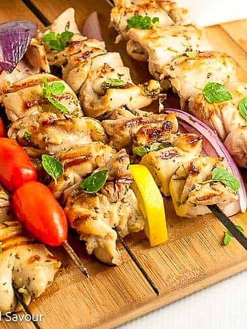 Greek lemon chicken kabobs on skewers on a board.