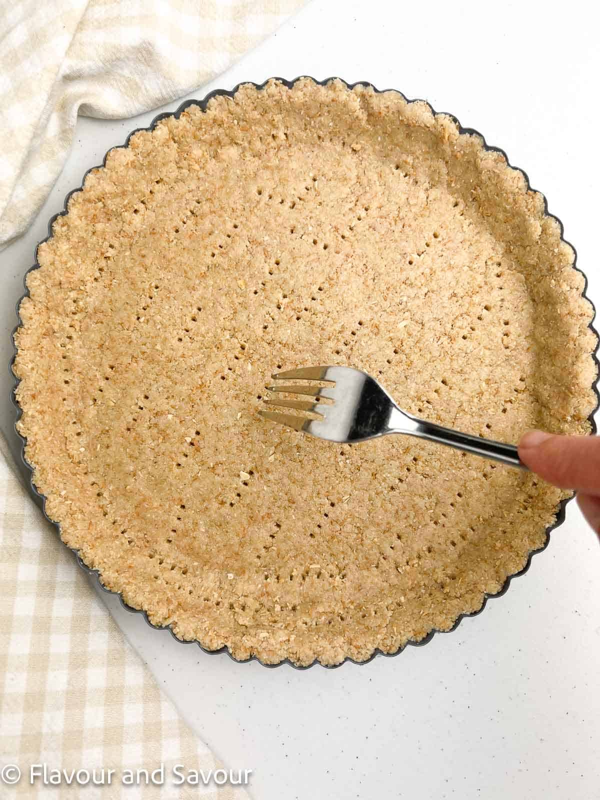 Pricking an almond flour tart crust with a fork.