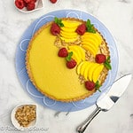 Overhead view of a mango tart decorated with mango slices, raspberries and mint leaves.