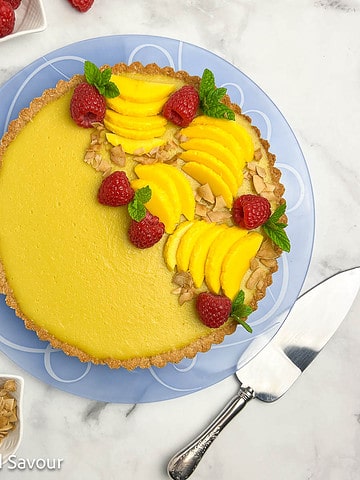 Overhead view of a mango tart decorated with mango slices, raspberries and mint leaves.