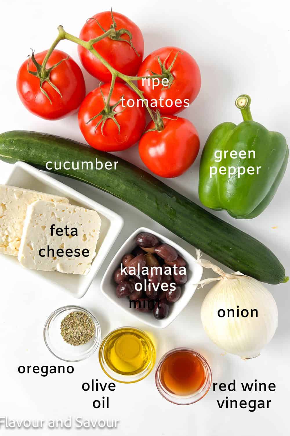 Labelled ingredients to make a traditional Greek salad:  tomatoes, cucumber, green pepper, feta cheese, kalamata olives, onion, dried oregano, olive oil and red wine vinegar.