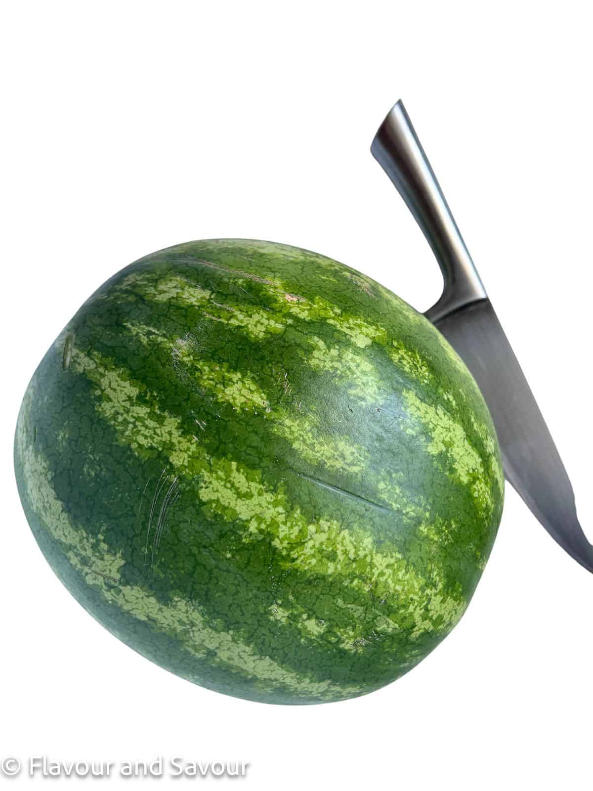 A whole watermelon with a knife beside it.
