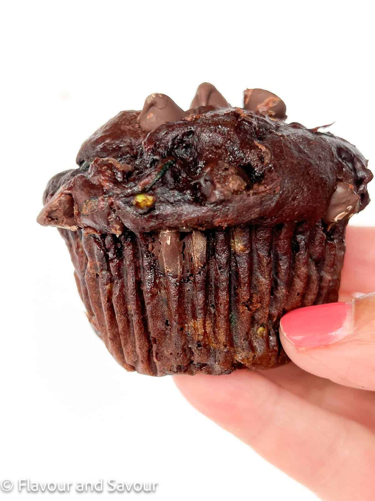 Close up view of a hand holding a single gluten-free double chocolate zucchini muffin.