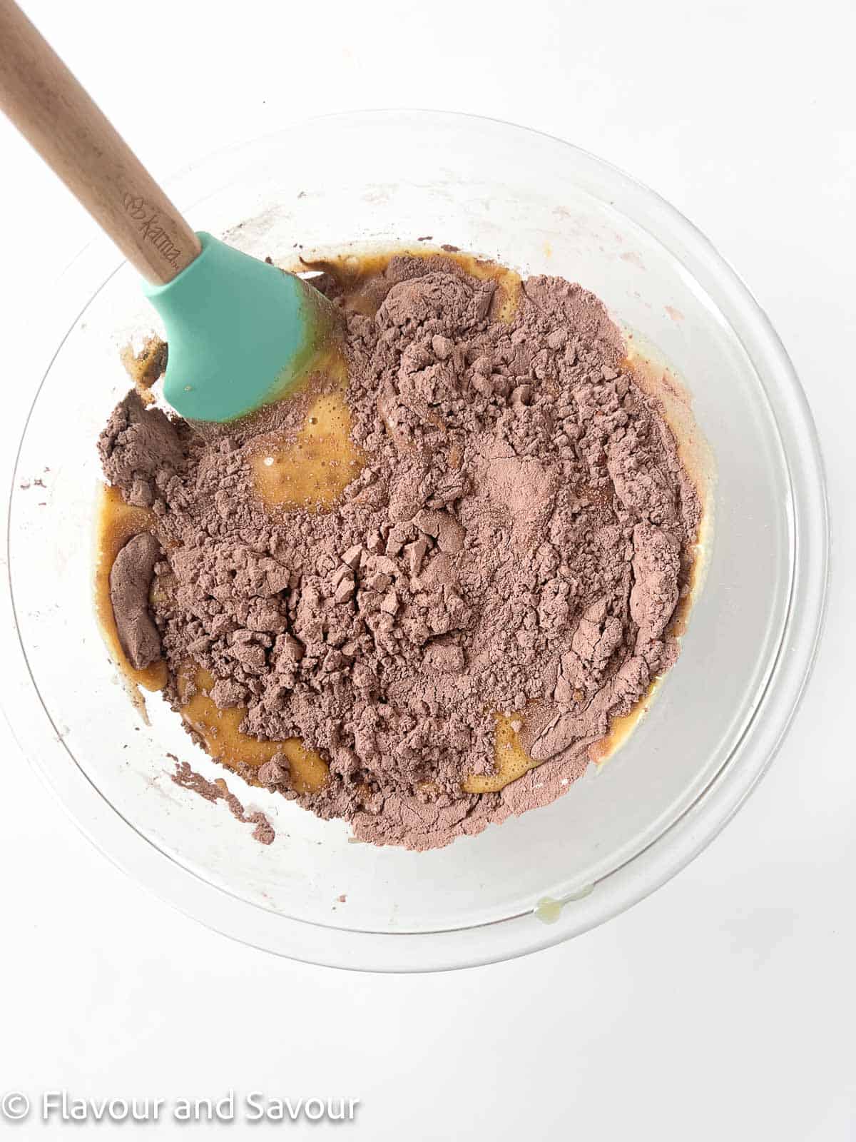 Wet and dry ingredients for chocolate zucchini muffins in a glass bowl with a spatula.